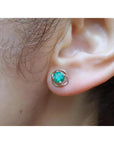Tulip emerald stud earrings with round green emeralds in 14K white gold, worn on an ear.