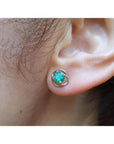 Tulip emerald stud earrings with round green emeralds in 14K white gold, worn on an ear.