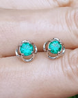 Colombian emerald stud earrings held between fingers.