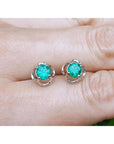Colombian emerald stud earrings held between fingers.