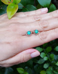 Hand wearing emerald tulip stud earrings with a green leafy background.