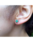 Tulip emerald stud earrings with round green emeralds in 14K white gold, worn on an ear.