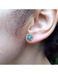Tulip emerald stud earrings with round green emeralds in 14K white gold, worn on an ear.