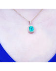 Emerald-cut Colombian emerald pendant with diamond halo on a 14k yellow gold chain, worn on a neck.