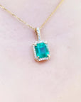Emerald pendant on a gold chain against a light pink skin background