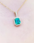 Emerald pendant on a gold chain against a light pink skin background