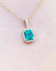 Emerald pendant on a gold chain against a light pink skin background