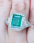 Toma cercana de un anillo con esmeralda cuadrada y diamantes rodeándolo hecho en oro blanco,