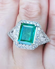 Toma cercana de un anillo con esmeralda cuadrada y diamantes rodeándolo hecho en oro blanco,