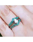 Close-up of a hand wearing an emerald enhancer ring with a central solitaire teardrop diamond ring.