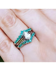 Close-up of a hand wearing an emerald enhancer ring with a central solitaire teardrop diamond ring.