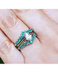 Close-up of a hand wearing an emerald enhancer ring with a central solitaire teardrop diamond ring.
