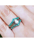 Close-up of a hand wearing an emerald enhancer ring with a central solitaire teardrop diamond ring.