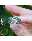 Hand holding a natural emerald enhancer ring with a blurred green leafy background.