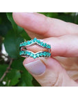 Hand holding a natural emerald enhancer ring with a blurred green leafy background.
