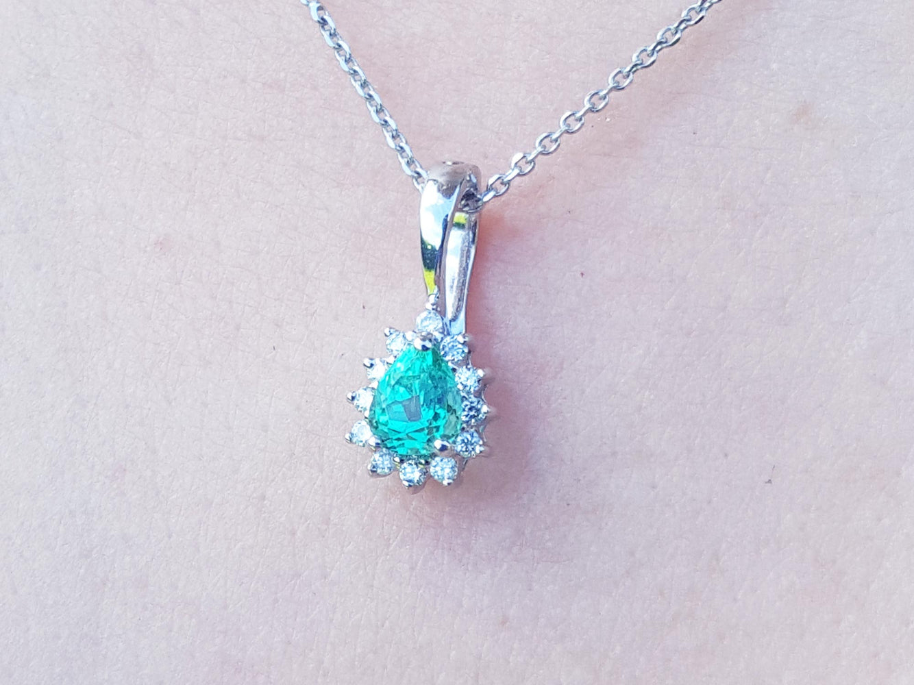 A white gold necklace with a teardrop emerald pendant on a light skin background.