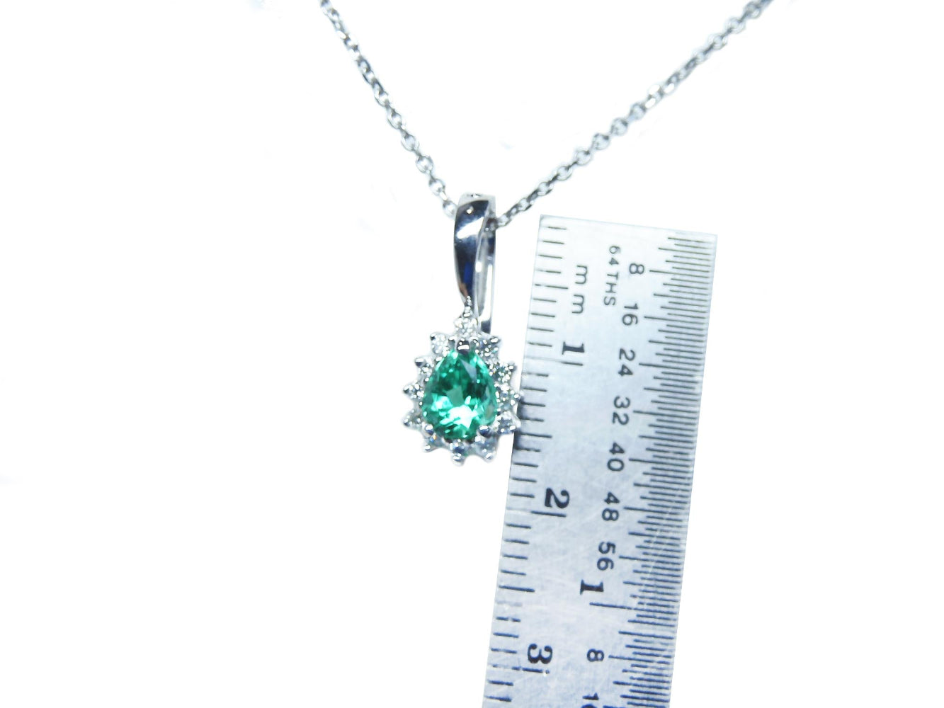 Colombian emerald enhancer pendant on a chain with a ruler for scale on a white background.