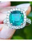 sostenido entre dedos un anillo con esmeralda corte cojín rodeado de diamantes en oro blanco para dama.