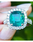 sostenido entre dedos un anillo con esmeralda corte cojín rodeado de diamantes en oro blanco para dama.