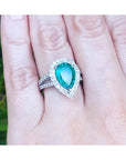 Anillo de oro blanco con una esmeralda corte pera rodeada de diamantes exhibido en una mano.