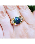 Men's 14K yellow gold ring with a vibrant oval Ethiopian black opal and two square accent stones.