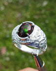 Silver ring for men with a colorful Welo black opal held against a blurred green background