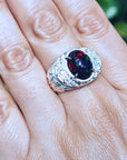 Men's silver ring with a red Welo black opal on a hand against a blurred green background