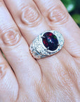 Men's silver ring with a red Welo black opal on a hand against a blurred green background