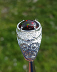 Men's silver ring with a red Welo Ethiopian black opal on a blurred green background