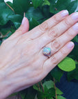 Hand wearing a colorful Ethiopian opal ring with green leaves in the background