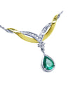 A far view of a white and yellow gold pendant necklace with a natural teardrop emerald dangling on a white background