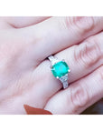 1.90 carat cushion cut emerald ring with trapezoid side diamonds in 18K white gold on a hand.