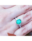 1.90 carat cushion cut emerald ring with trapezoid side diamonds in 18K white gold on a hand.