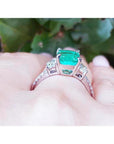 18K white gold ring with a cushion cut emerald and trapezoid side diamonds on a hand.