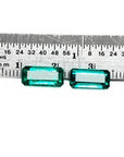Two emerald-cut, medium deep bluish-green natural emeralds, a matching pair, displayed against a ruler.