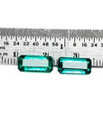 Two emerald-cut, medium deep bluish-green natural emeralds, a matching pair, displayed against a ruler.