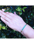 Hand wearing a five stone emeralds and diamonds bracelet with a green leafy background.