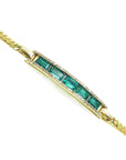 Gold bracelet with emeralds and diamonds on a side profile view.