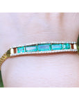 A five stone emerald bracelet natural Colombian emeralds fine quality yellow gold on a wrist against a blurred natural background.