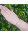 Flexible 14K yellow gold bangle bracelet with genuine emeralds and accent diamonds on a hand.