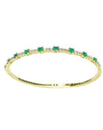 Flexible 14K yellow gold bangle with oval emeralds and accent diamonds.