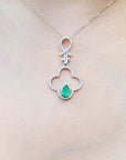 A white gold necklace with an emerald gemstone pendant on a person wearing a black top.
