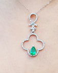 A white gold emerald pendant with accent diamonds on a beige skin background.