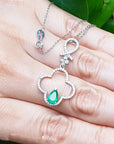 A four-leafe pendant with an emerald gemstone on a hand, brand 'Emeralds & Jewelry Corp.' visible