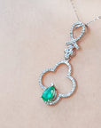 A white gold necklace with a four-leafe pendant and emerald gemstone on a beige background.
