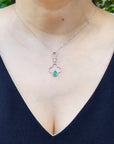 Necklace with a emerald pendant worn by a woman against a blurred natural background.