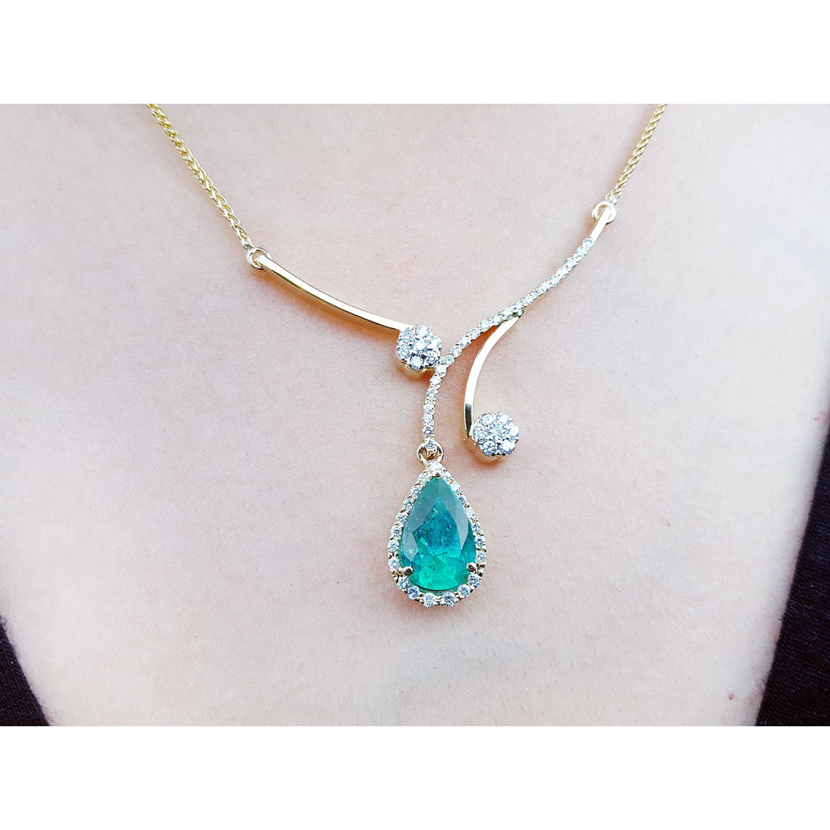 Frontal close view of a necklace with a teardrop-shaped emerald gemstone pendant on a lady's collar