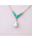 14K gold necklace with a 0.69 ct pear diamond and 0.35 ct round emeralds in a V-shape.