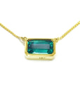 East-west rectangular emerald solitaire necklace in 18K yellow gold with a vibrant bluish-green stone.