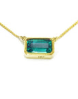 East-west rectangular emerald solitaire necklace in 18K yellow gold with a vibrant bluish-green stone.